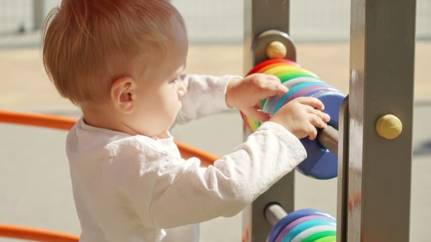 Portrait of little boy spinning colorful circles on abacus at playground. Children developments, kids education, baby learning Royalty-Free Stock Footage #1102176035