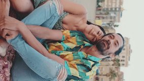 VERTICAL VIDEO: Happy couple sitting hugging on blanket on the beach