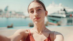 Сlose-up young woman takes a selfie, video call sitting at the seaport uses a mobile phone. Smiling girl Use Social Media, Streaming Service in the background yachts and ships