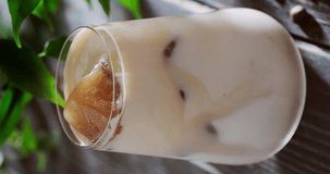 Iced coffee latte in drinking glass, refreshing cocktail with brown coffee ice cubes, person squeezing canned whipped cream from spray, slow motion close up video clip, 4k footage