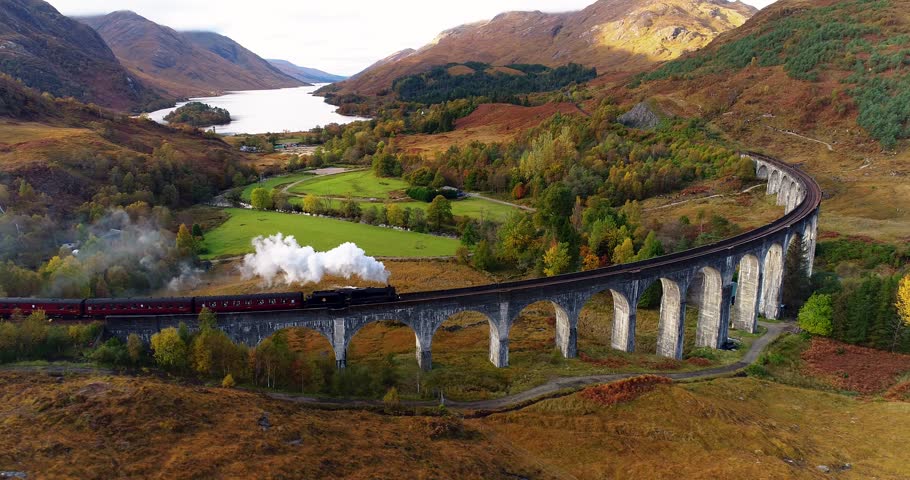 Aerial push in towards Glenfinnan Viaduct with Jacobite Steam train crossing it Royalty-Free Stock Footage #1102184039