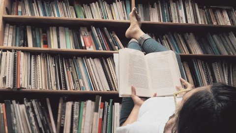 Hispanic woman reading laying on the floor of the library. 4k