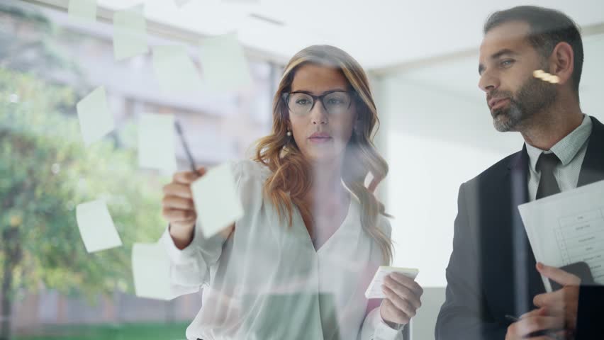 Video of successful business couple team writing on stickers at office glass board while discussing together in a modern office | Shutterstock HD Video #1102185645