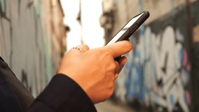 Young Woman Using Mobile Phone at Ghetto Alleyway with Graffiti on Background. Female Hands Texting on Smartphone, Natural Golden Hour Sunset Light 4K Slow Motion Close Up, Thailand. - Powered by Shutterstock - Get 15% off with code: PIKWIZARD15