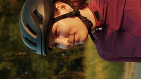 Woman in black cycling helmet drinking water or isotonic drink after bike ride at sunset. Vertical video. Pro female cyclist drinks water from bottle after intense cycling training. Cardio workout