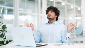 Young developer meditating with closed eyes during a break while sitting at the workplace in the office. A calm worker rests and relaxes. The male takes a break to relieve stress. Feels peace of mind - Powered by Shutterstock - Get 15% off with code: PIKWIZARD15