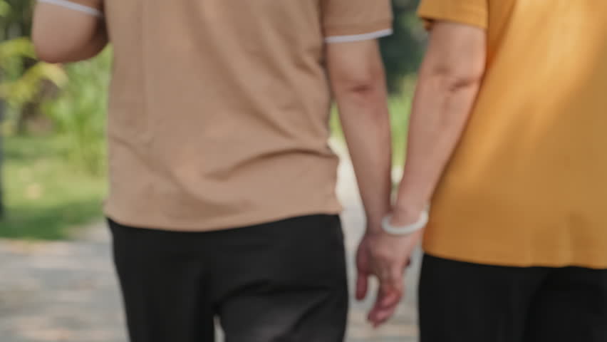 Back view of family couple walking together in park on summer day, holding badminton rackets and chatting