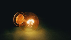 Yellow Incandescent Lamp Lights Up, Flickers on a Green Background in Dark Room. Close up. Tungsten light bulb with warm blinking light pulsates, lies on table. Power outage, power failure. Crisis. - Powered by Shutterstock - Get 15% off with code: PIKWIZARD15