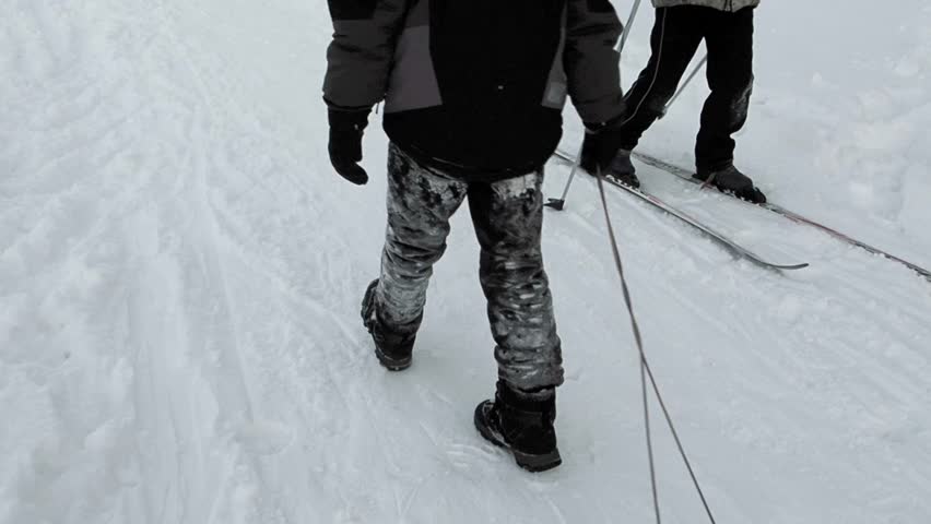 happy boys in dark clothes  are hesitantly walking on colorful skis in winter.Children learn to ski in a snowy park and have fun.Beautiful snowy winter with pure sparkling snow.Boy walking with a sled