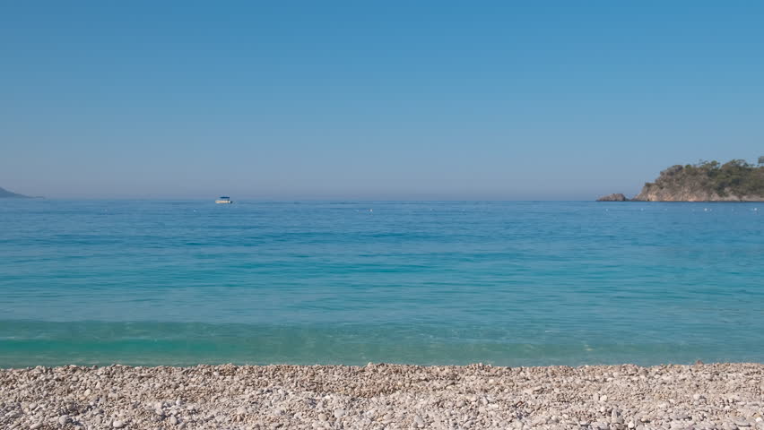 Child admire turquoise sea on shore. An alone little girl walk along the pebbles shore by the turquoise sea water under the sun.
