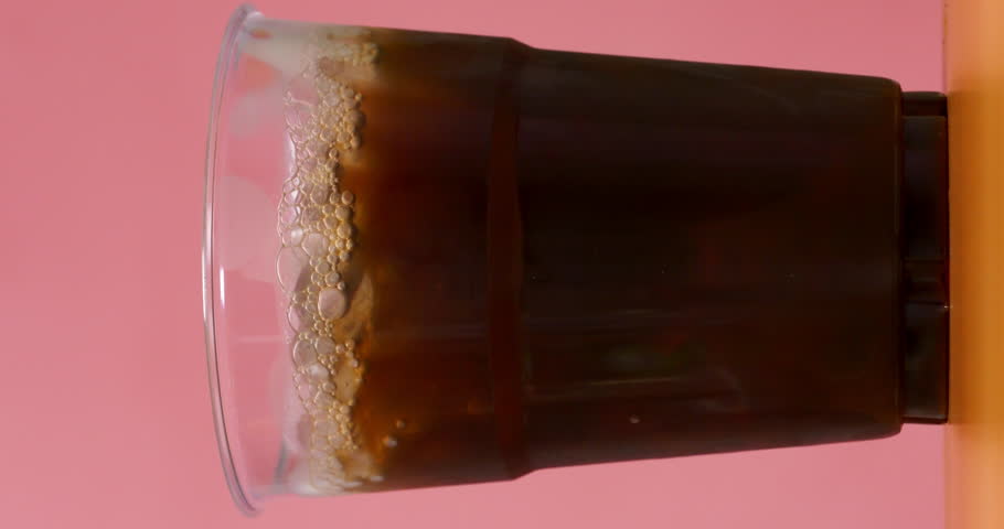 4K footage vertical video Front view SLO MO CU, coffee cup pouring coffee into a glass with ice.