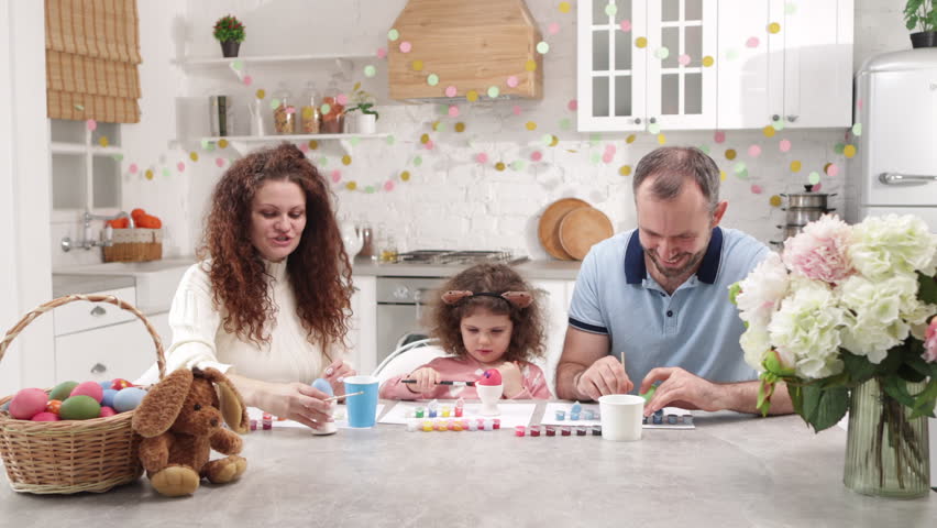 Portrait of lovely family decorating traditional Easter eggs with their cute, little daughter. Laughing, happy mother and father helping their girl to paint Easter symbols. High quality 4k footage