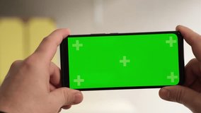 Man hands holding green screen chroma key smartphone in office. Person using Internet, social media, online shopping with mobile phone device without keying close up