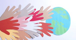 Vertical video of hands with globe made of colourful paper on white background with copy space. Community, global, people and art.
