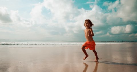 Boy run barefoot on the beach with smile and laugh, slow motion: film stockowy