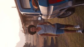 Vertical video portrait of smiling woman unloading backpacks from pick up truck on road trip to cabin in countryside at sunset - shot in slow motion