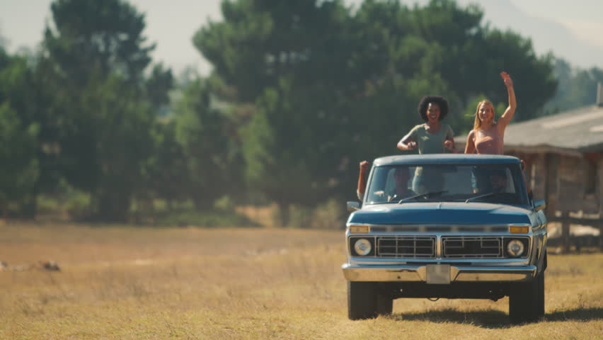 Two women standing up in back of pick up truck waving as friends enjoy road trip through countryside - shot in slow motion Royalty-Free Stock Footage #1102211039