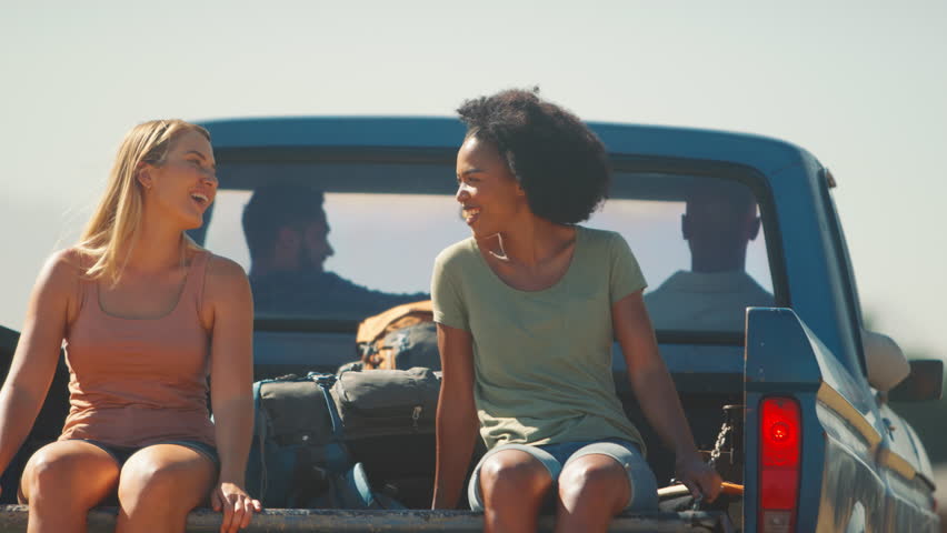 Two women riding in back of pick up truck as friends enjoy road trip through countryside - shot in slow motion Royalty-Free Stock Footage #1102211045