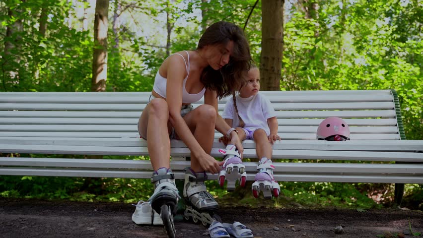Mother and daughter taking off inline roller on bench after skating in public park together. Family leisure sport activity weekend.