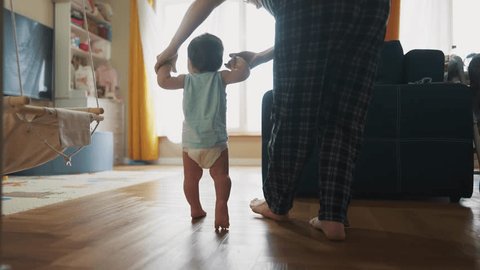 baby takes first steps to learn. happy family kid dream concept. mom teaches baby newborn to walk and take light first steps. mom holding baby hands teaches to walk silhouette from window วิดีโอสต็อก