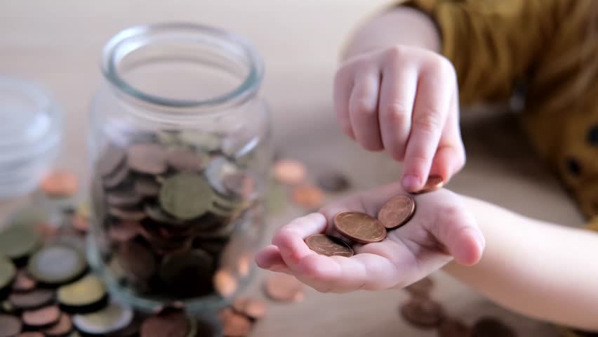 close-up of hands of small child manipulate with metal coins, kid counts, puts euro union money in piggy bank, glass jar, concept of pocket money, life insurance, save up for gift Royalty-Free Stock Footage #1102223525