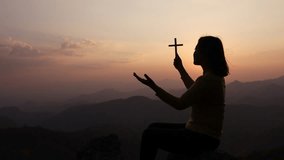 Silhouette of faithful woman praying with Christian cross at sunset as concept for religion, faith, prayer and spirituality, Video 4k slow motion.