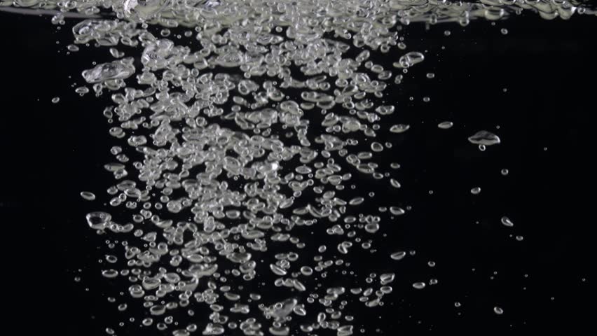 Air bubbles in mineral water rise up over black background. Slow motion of opening carbonated drink