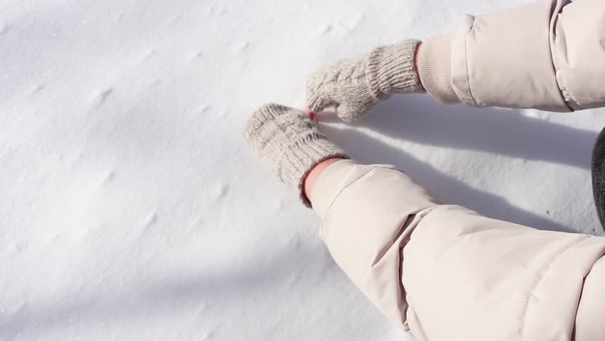 A woman's hand draws a Heart on the Snow in Knitted Gloves on a Sunny Day. Valentine's Day, Love and Dating, Winter Holidays concept. Close-up, slow motion. | Shutterstock HD Video #1102231767