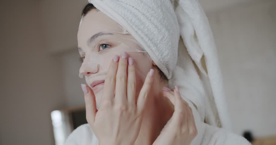 Beauty shot of young woman wearing paper sheet facial mask ready for moisturizing anti wrinkle day or night cream at home. Beautiful woman applying moisturizing mask. healthcare, wellness, wellbeing. Royalty-Free Stock Footage #1102237331