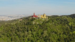 Flying drone footage Pena palace touristic place famous mansion construction castle tower in Sintra region Portugal green forest landscape hilly mountain sunny day panorama of Europe aerial top view