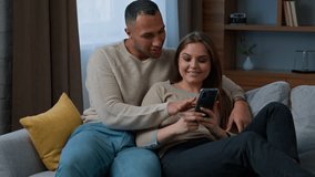 Multiracial couple customers relax on sofa use mobile phone at home diverse woman wife and man husband talk make order online delivery buy internet goods shopping in e-commerce app look at cellphone - Powered by Shutterstock - Get 15% off with code: PIKWIZARD15