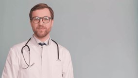 Doctor shows and presents something with his hand, isolated on gray background. 4k video