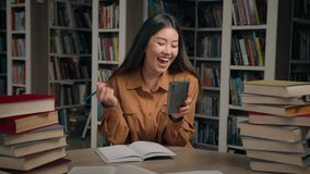 Asian woman student preparing for exam in university library writing notes doing homework happy girl winner get notification on phone read good news celebrate victory success high academic achievement - Powered by Shutterstock - Get 15% off with code: PIKWIZARD15