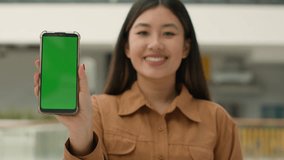 Asian chinese woman hold smartphone in front show mobile phone with green screen mockup advertisement digital app advertise cellphone web service korean girl point finger at empty chroma key display