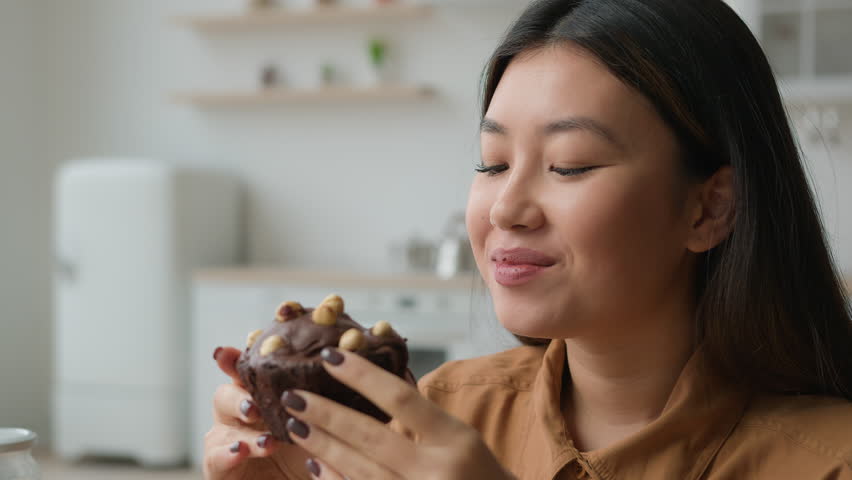 Asian chinese korean japanese girl hungry woman chewing cupcake with pleasure eat sweet cake with nuts eating dessert at home kitchen fresh bakery delivery food enjoy brownie overweight calorie weight Royalty-Free Stock Footage #1102243417