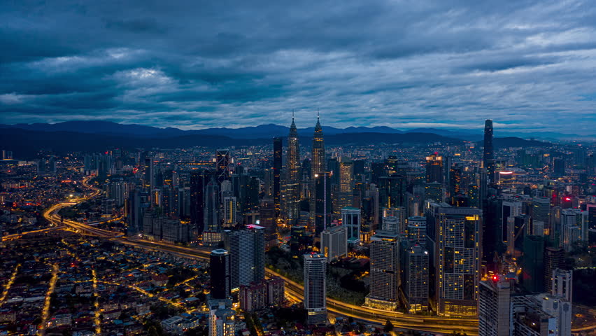 Aerial Drone Time lapse: High angle drone view during a cloudy dawn overlooking Kuala Lumpur city skyline against mountains background in Malaysia. Tilt up motion timelapse. Prores 4KUHD