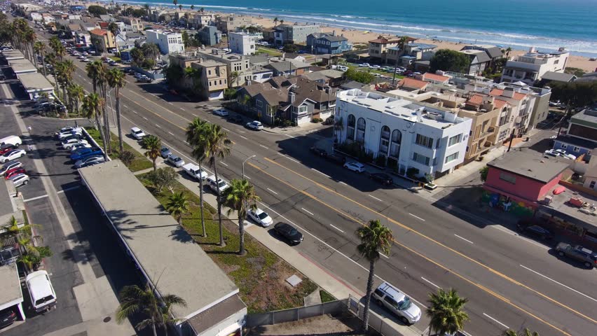 aerial footage of cars and trucks driving on the street with palm trees, homes, apartments blue ocean water and a sandy beach at Rosie's Dog Beach in Long Beach California USA