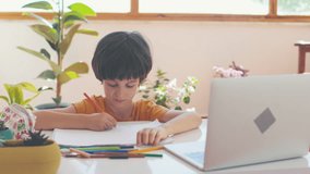 child draws in an album during an online lesson, sitting in front of a laptop. Slow motion. distance learning. occupation at school.
