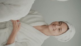 Vertical Video.Back View of Smiling Woman Looks in the Mirror and Applying Cream. A Happy Young Woman with a White Towel on Her Head Cares About Her Skin at Home.Beauty and health.