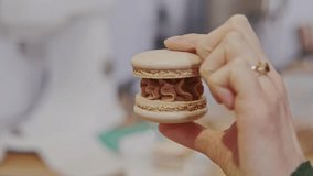 Close up video of woman hand holding tasty macaroon over kitchen background