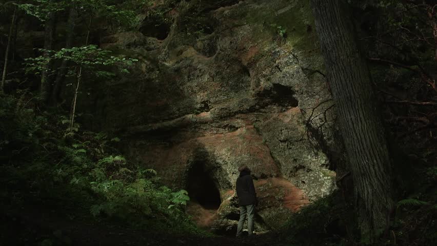 dolly shot of a man standing in front of a sandstone rock with a cave