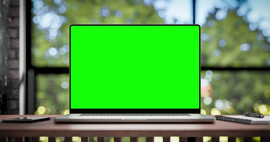 Laptop with blank green screen. Static footage with trees swaying or moving in the wind. Home interior or loft office background, 4k 30fps, looped video