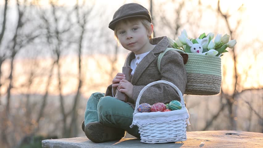 Beautiful stylish toddler child, boy, playing with Easter decoration in the park, springtime on sunset