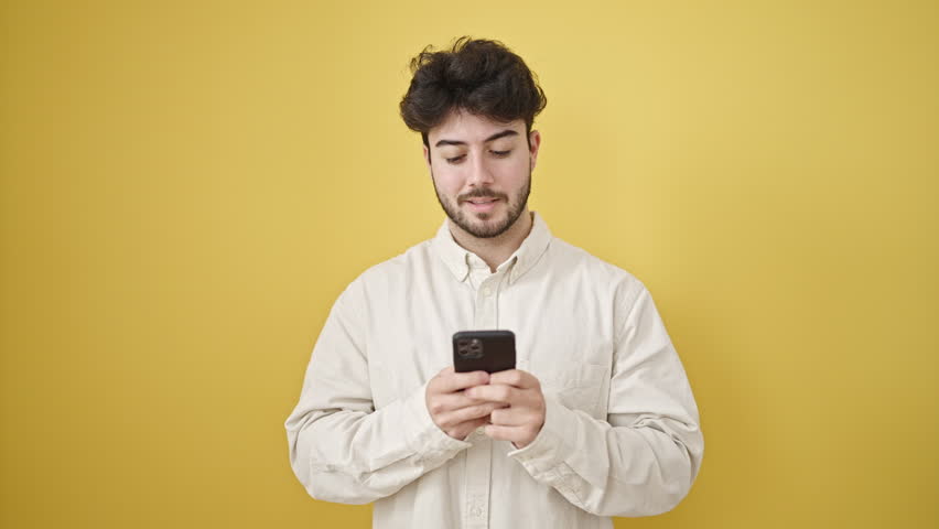 Young hispanic man using smartphone smiling over isolated yellow background