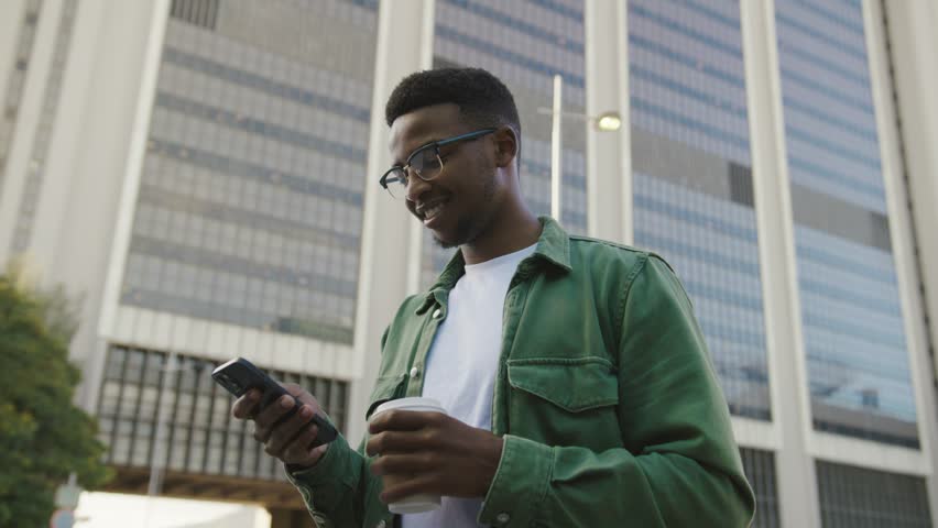 Happy young black man in casual clothing having video call on mobile phone in street Royalty-Free Stock Footage #1102264131