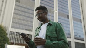 Happy young black man in casual clothing having video call on mobile phone in street