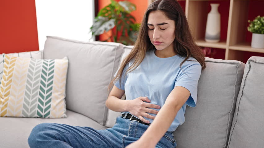 Young beautiful hispanic woman suffering for stomach ache sitting on sofa at home Royalty-Free Stock Footage #1102264217