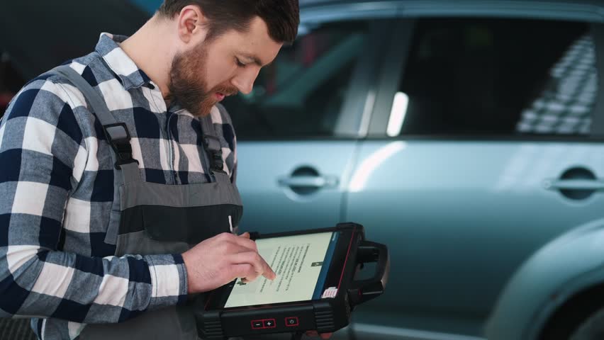 Reading the instruction by using tablet. Man is repairing the car at a service station. Royalty-Free Stock Footage #1102265213