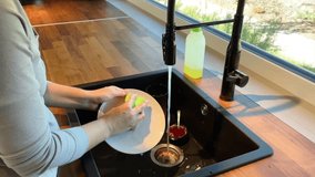 A woman is washing dishes in the kitchen. Cup and washing sponge in the hand. Kitchen with window and street view. High quality video footage 