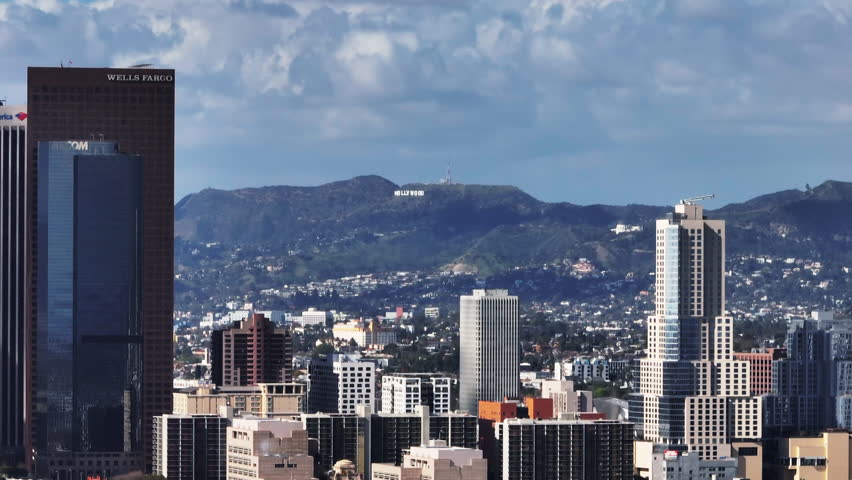 Distant view of Hollywood Sign in hills above city. Sliding reveal of modern skyscrapers in financial district. Los Angeles, California, USA